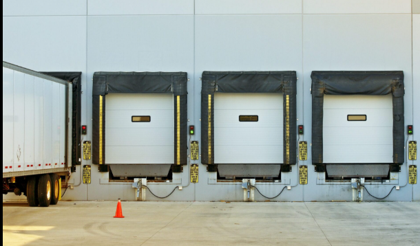 Four loading dock doors with black bumpers are aligned on a warehouse wall